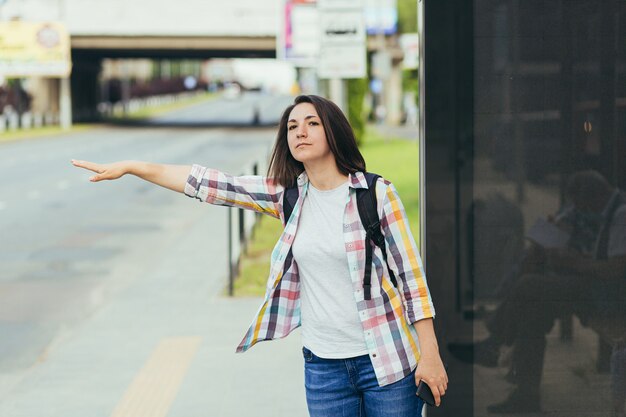 携帯電話のアプリを使ってバス停でタクシーに乗ろうとしている若い女性