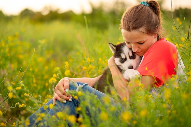 Young woman in a Tshirt hugs a husky puppy at sunset outdoors