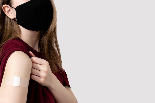 Young woman in tshirt showing plaster on shoulder after coronavirus vaccine copy space