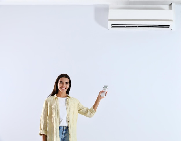 Young woman turning on air conditioner against white background