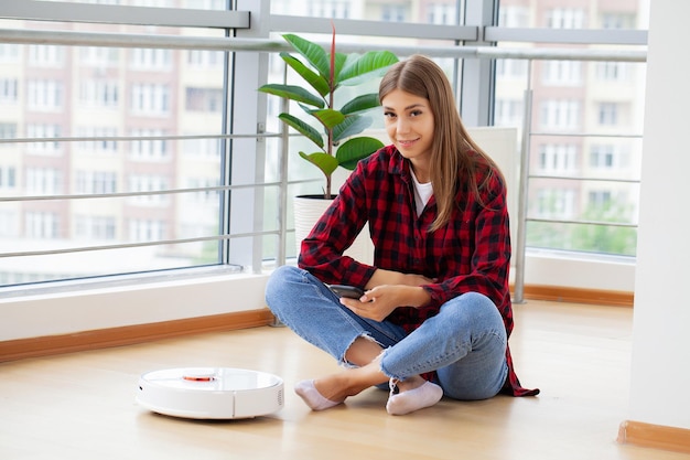 若い女性がスマート ロボット掃除機をオンにします。