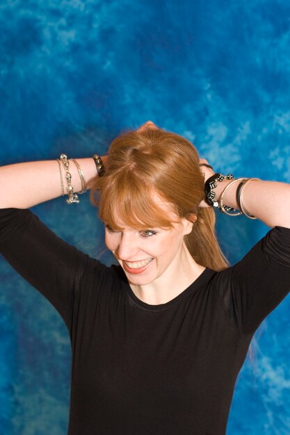 Young woman tying hair against blue wall