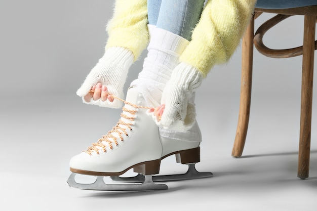 Young woman tying laces on ice skate shoes against grey