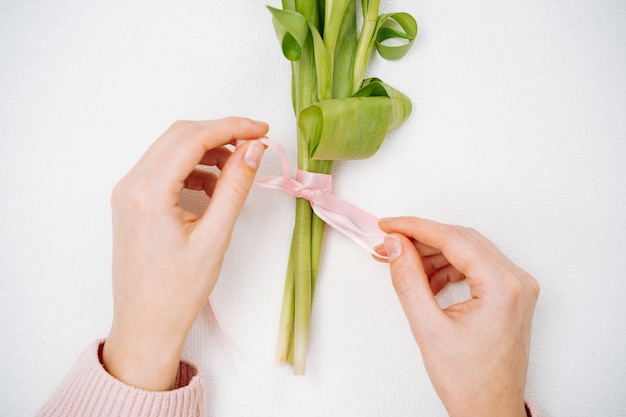 ピンクのチューリップの花束にリボンを結ぶ若い女性。上面図、白い背景、テキストコピースペース。