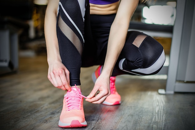 Young woman tying shoelaces before training in gym.