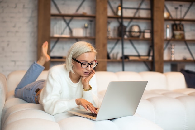 Young woman typing email on laptop computer lying on bed, send answer to business partner from home