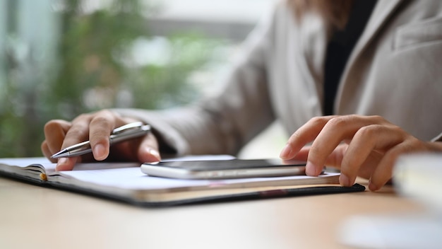 Young woman typing messages on mobile phone and writing notes