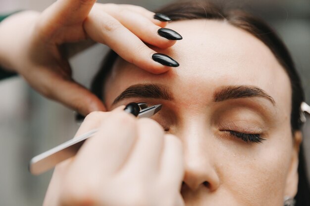 A young woman undergoes an eyebrow correction procedure in a beauty salon closeup the girl paints her eyebrows in the salon