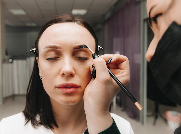 A young woman undergoes an eyebrow correction procedure in a beauty salon closeup the girl paints her eyebrows in the salon