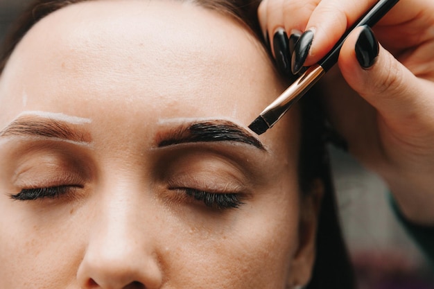 A young woman undergoes an eyebrow correction procedure in a beauty salon closeup the girl paints her eyebrows in the salon