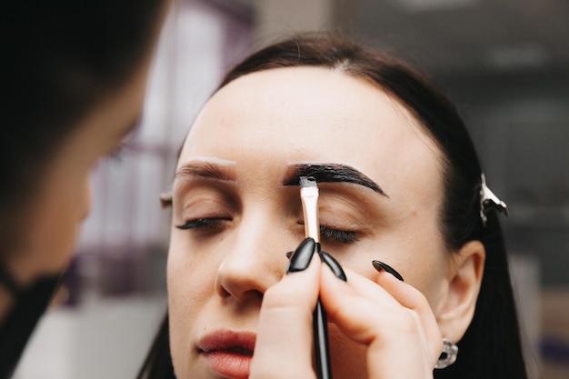 A young woman undergoes an eyebrow correction procedure in a beauty salon closeup the girl paints her eyebrows in the salon