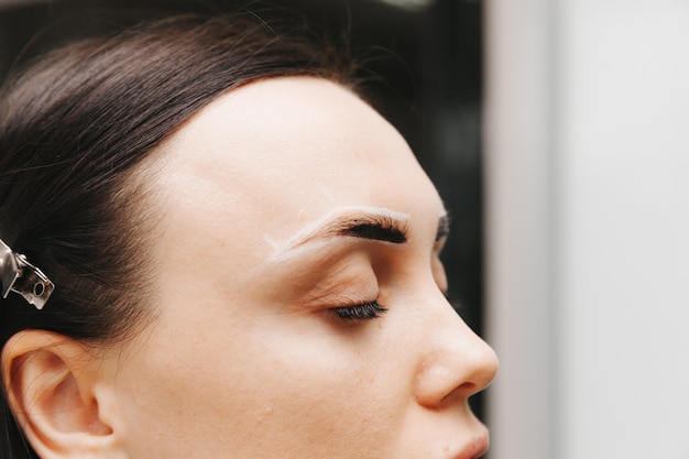 A young woman undergoes an eyebrow correction procedure in a beauty salon closeup the girl paints her eyebrows in the salon