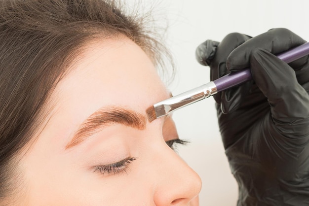 Young woman undergoing eyebrow correction procedure in beauty salon closeup Dying eyebrows whith brush