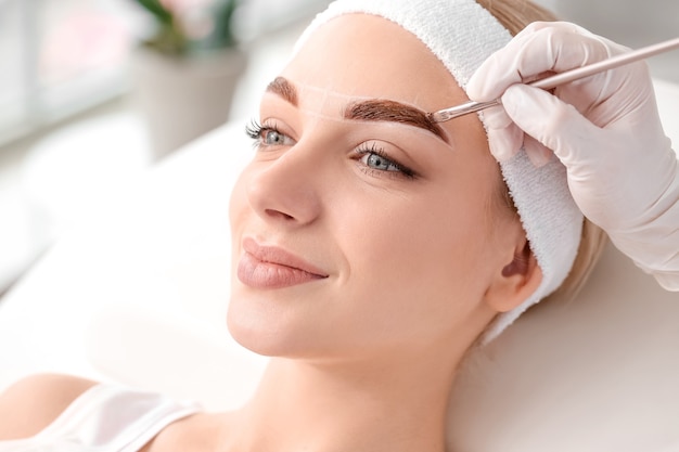 Young woman undergoing eyebrow correction procedure in beauty salon