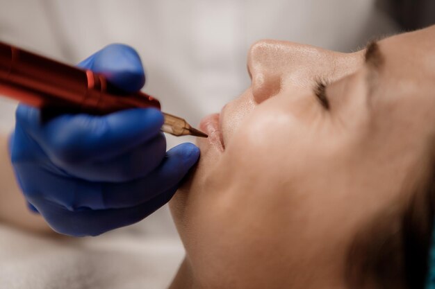 Young woman undergoing procedure of permanent lip makeup in tattoo salon closeup