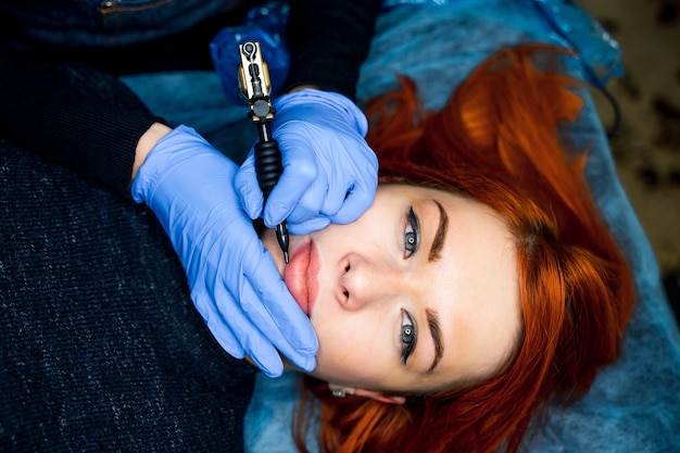 Young woman undergoing procedure of permanent lips makeup in tattoo salon, closeup