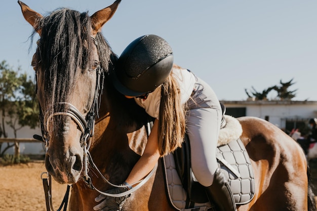 Young woman in uniform and on her horse embraces him affectionately