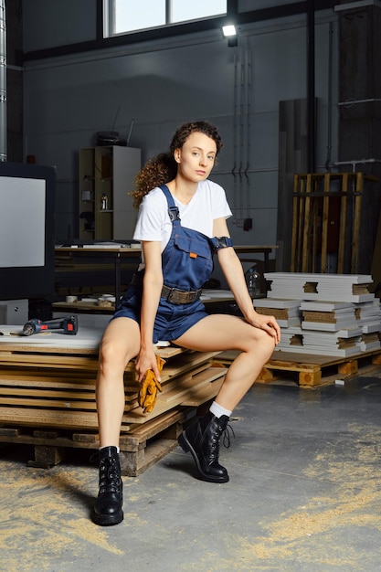 Photo young woman in uniform sits on a stack of chipboard slabs