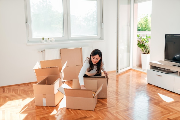 Photo young woman unpacking cardboard boxes at new home.