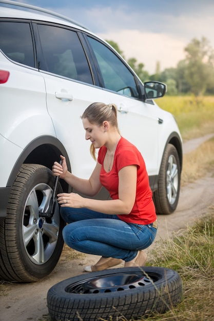 若い女性がフィールドで車のパンクしたホイールのナットを緩めます