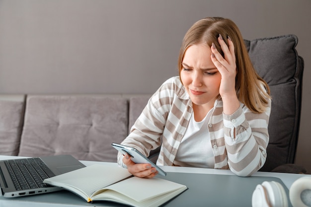 Giovane donna sconvolta sotto stress. la donna confusa che tiene la testa ha ricevuto cattive notizie tramite smartphone al lavoro. la ragazza teenager esamina lo schermo dello smartphone durante la depressione di emozioni negative di lavoro o istruzione online.