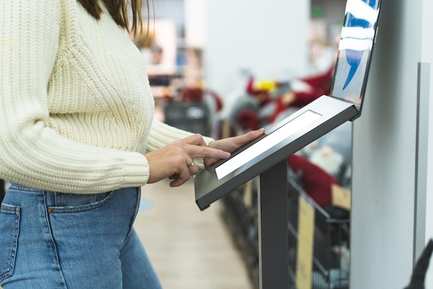 Молодая женщина использует электронный дисплей в магазине, соблюдая безопасное расстояние от других в магазине