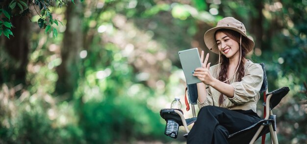 Молодая женщина использует видеозвонок с планшета во время кемпинга в парке