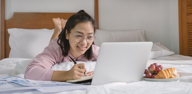 Young woman used laptop video conferences and eating fruits on the bed, healthy food and work from home concept.