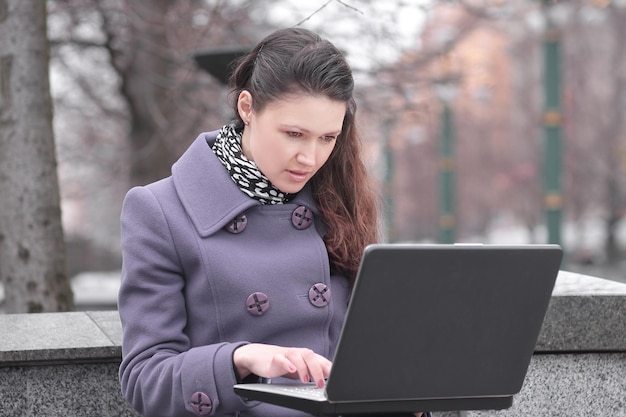 Young woman uses laptop sitting on bench in city park