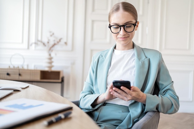 若い女性がオフィスで電話を使用し、メールのメッセージを読みます