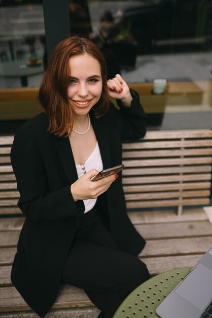 Фото Молодая женщина пользуется телефоном в уличном кафе