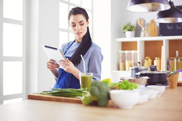 写真 彼女の台所で料理するためにタブレットコンピュータを使用している若い女性