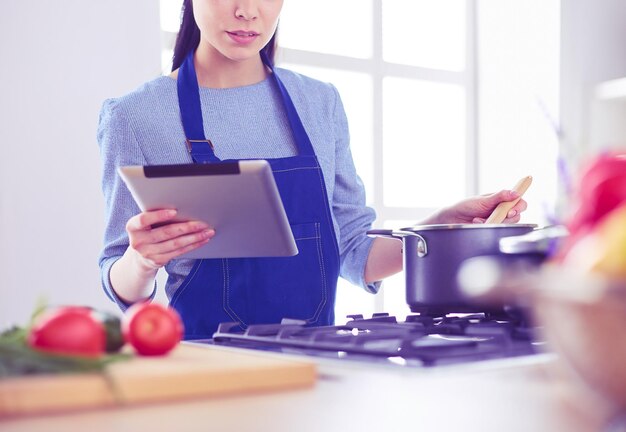 写真 彼女の台所で料理するためにタブレットコンピュータを使用している若い女性