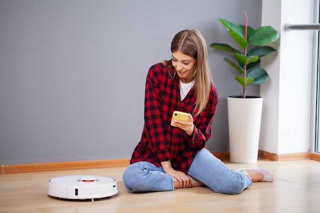 Young woman using automatic vacuum cleaner to clean the floor.