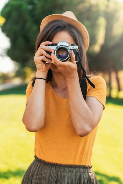 公園で写真を撮るためにカメラを使用して若い女性。