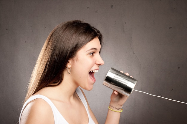 Young woman using a can as telephone on a gray background