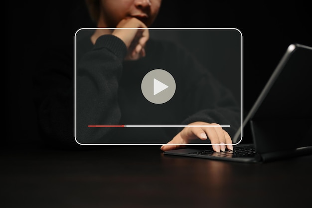 仮想画面上の再生ボタンでオンラインビデオストリーミングを見るためにコンピューターのタブレットを使用している若い女性。