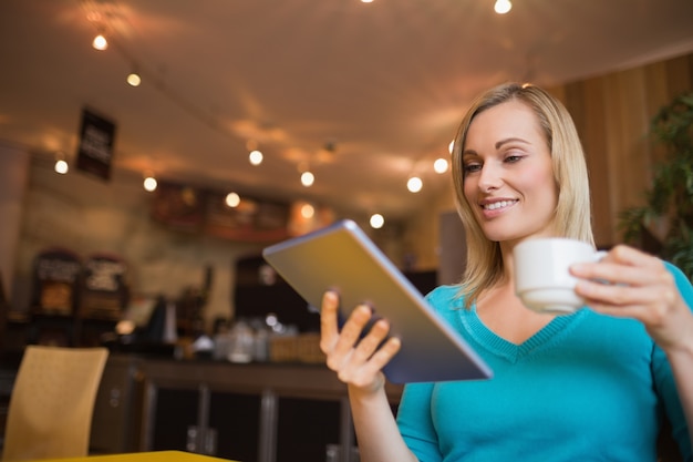 Young woman using digital tablet while holding cup