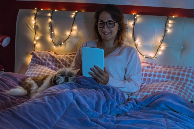 Young woman using digital tablet while sitting on bed at home