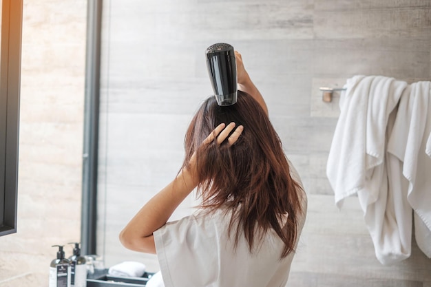 Photo young woman using hair dryer at home or hotel hairstyles and lifestyle concepts