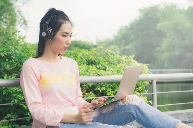 公園に座っているときにヘッドフォンとラップトップを使用する若い女性