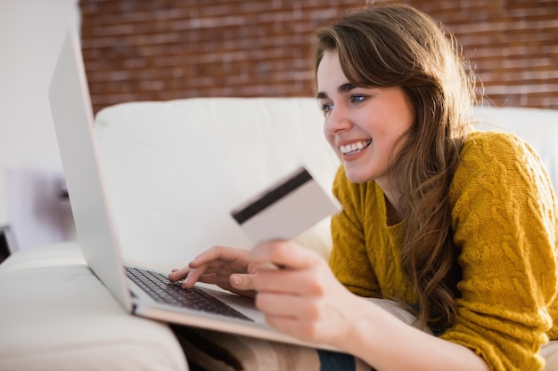 Young woman using her credit card to buy online sitting on the couch at home