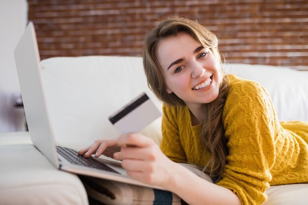 Young woman using her credit card to buy online sitting on the couch at home