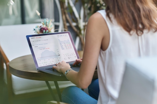 Young woman using her laptop while sitting at a table in a cafe rear view