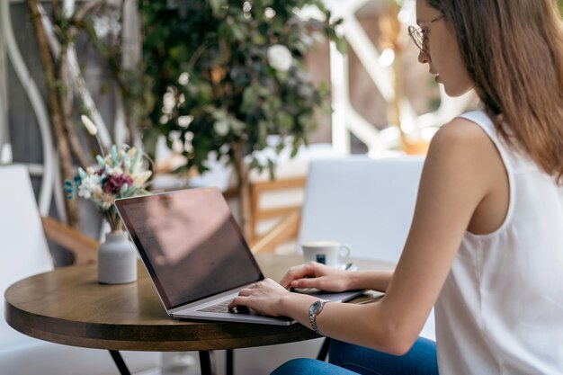 Young woman using her laptop while sitting at a table in a cafe rear view