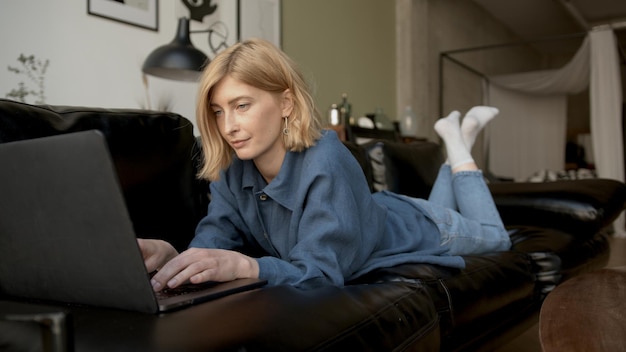 Giovane donna che usa il laptop che si rilassa su un divano in soggiorno donna in jeans vestiti concentrati messaggi di testo su un dispositivo concetto di tempo libero e lavoro da casa