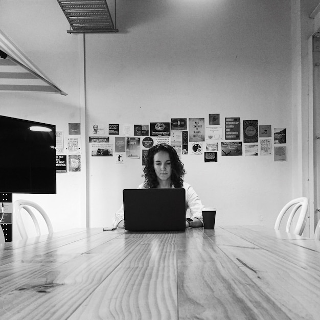 young woman using laptop at table against wall