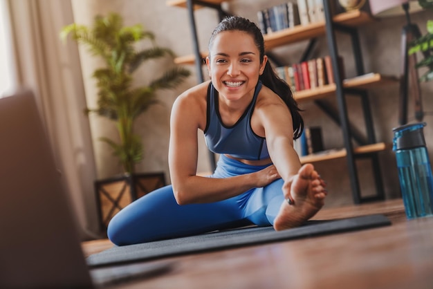 Photo young woman using laptop for watching videos with online instructions doing stretching exercises