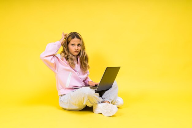 Foto giovane donna che usa il portatile mentre è seduta sul divano sullo sfondo giallo