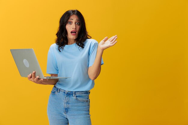 Young woman using laptop while standing against yellow background